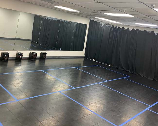 A spacious dance studio with wooden flooring, mirrored walls, and black curtains arranged along one side.