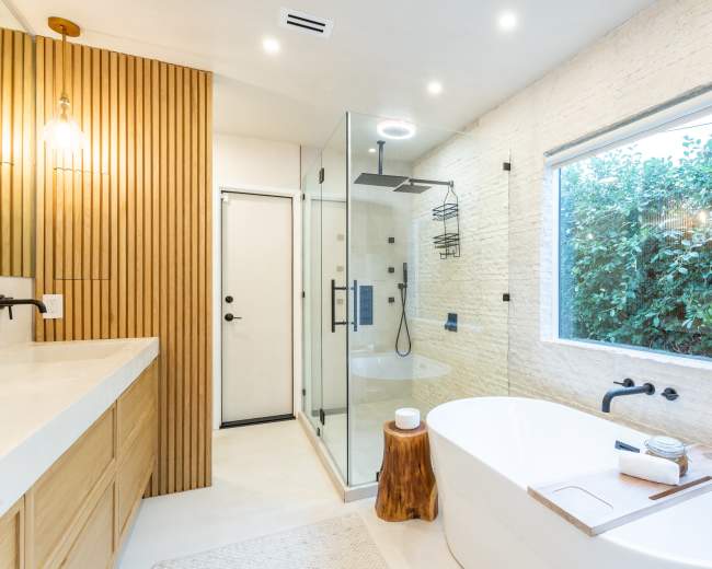 The image shows a modern bathroom featuring a freestanding bathtub, a glass shower enclosure, and wood accents on the walls.