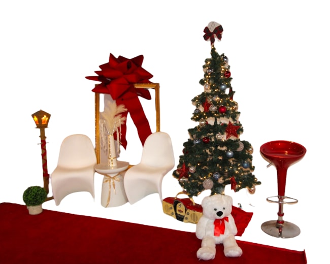 A Christmas scene featuring a decorated tree, a pair of white chairs, a red bow, a lamp post, and a white teddy bear on a red carpet.