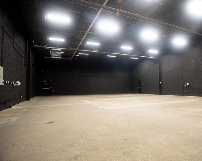 The image shows a large, empty industrial space with black walls and bright overhead lights.