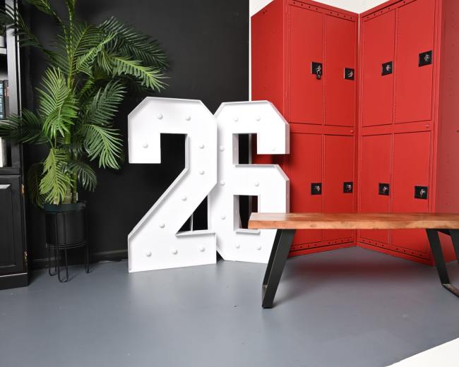 The image features a large white marquee number "26" next to red lockers and a wooden bench with black metal legs in a minimalistic interior setting.