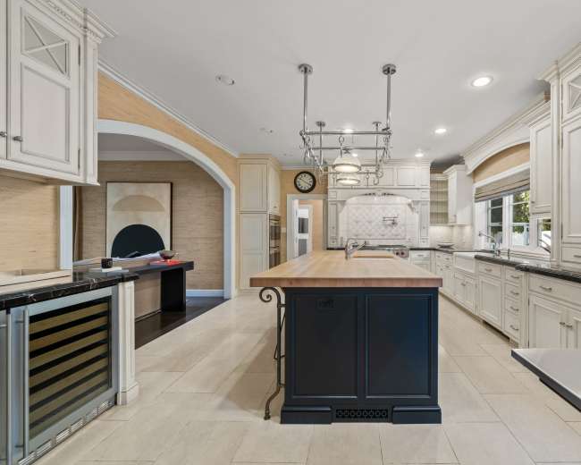 The image shows a spacious kitchen featuring an island with a wooden countertop, white cabinetry, and modern appliances.