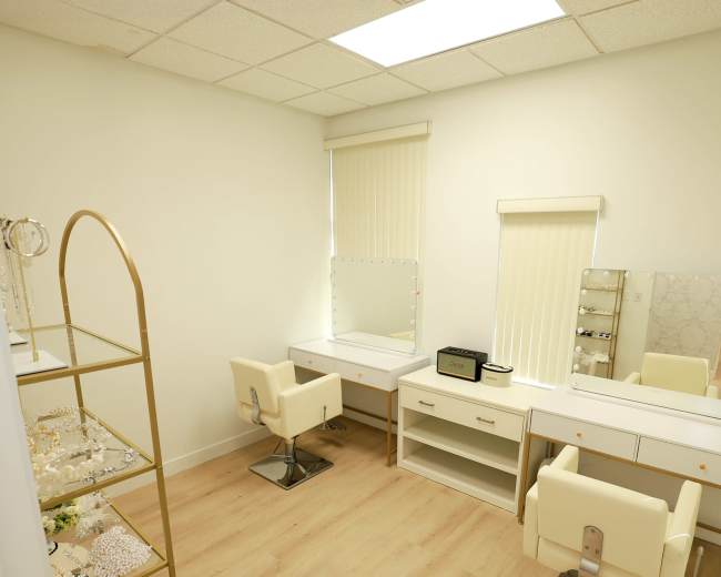 The image shows a bright room featuring a vanity area with two chairs, a mirror, and a display shelf for jewelry.