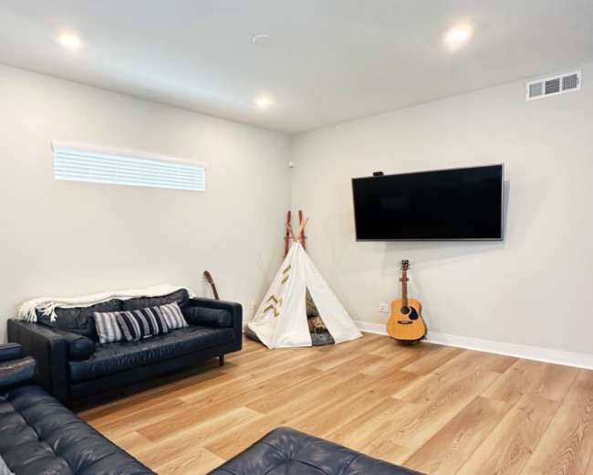 The image features a modern living room with a leather sofa, a television mounted on the wall, a teepee, and an acoustic guitar leaning against the wall.