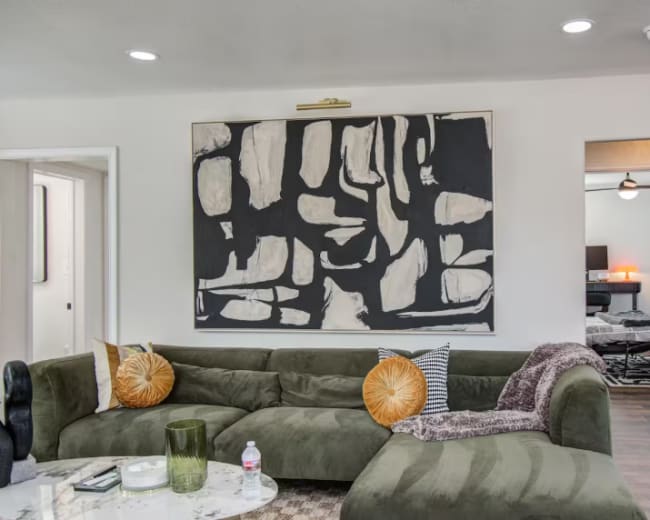 The image shows a modern living room with a green sectional sofa, a round coffee table, and an abstract black and white artwork on the wall.