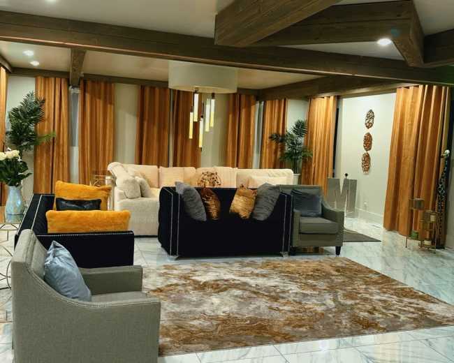 The image shows a modern living room with a mix of seating options, a large area rug, and elegant curtains, creating a cozy atmosphere.