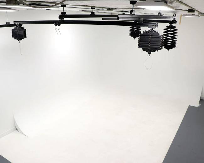 A well-lit photography studio with a seamless white backdrop and overhead lighting fixtures.