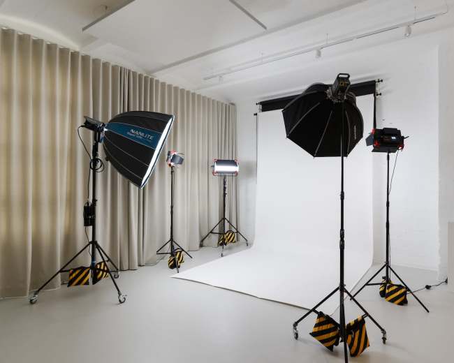 The image shows a photography studio equipped with various lighting setups and a blank backdrop.