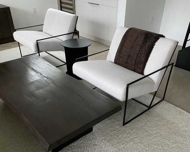 The image shows a cozy living area featuring two modern armchairs with a small side table and a large wooden coffee table on a textured area rug.