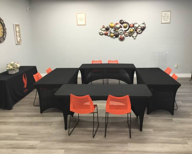 A meeting room is set up with black tables arranged in a U-shape and orange chairs positioned around them.