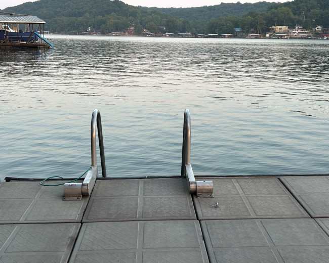 A set of metal steps leads into calm water from a wooden dock by the shore.