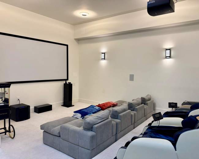 The image depicts a home theater with a large screen, a sectional sofa, and a few chairs arranged for seating.