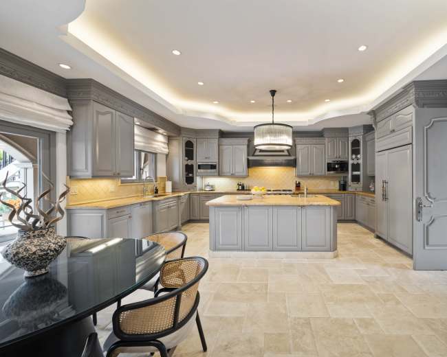 The kitchen features gray cabinetry, a central island with a sink, and a light-colored stone floor.