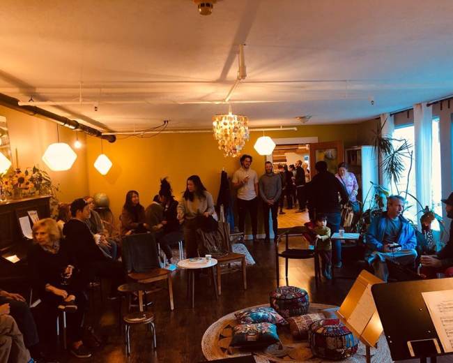 A group of people socializes in a cozy, dimly lit room adorned with plants and decorative lighting.