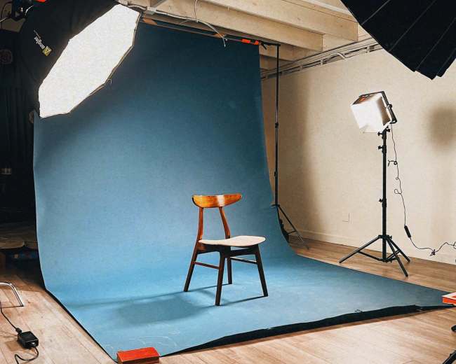 A wooden chair is positioned on a blue backdrop in a well-lit photography studio.