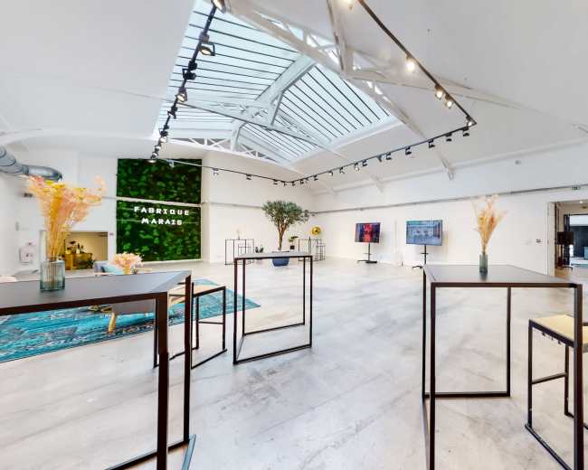 The image shows a modern, spacious interior with tall ceilings, large windows, and minimalist furniture arranged around the room.