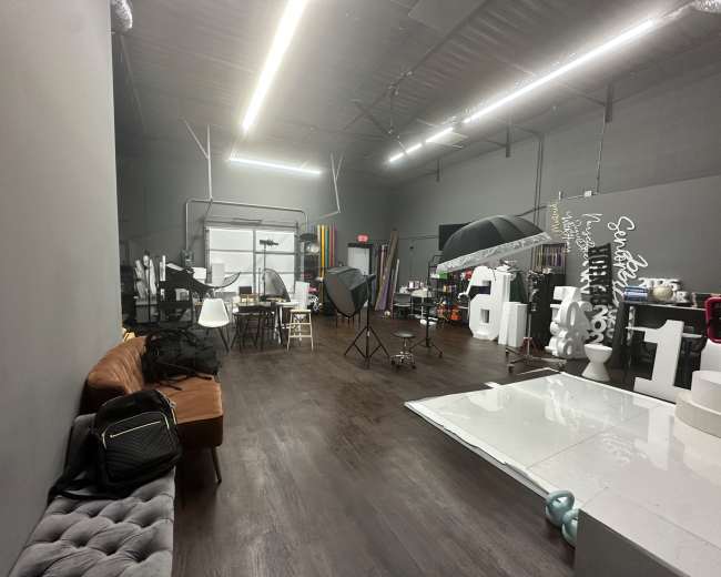 The image shows a spacious studio with various photography equipment, a seating area, and different props set up for a photoshoot.