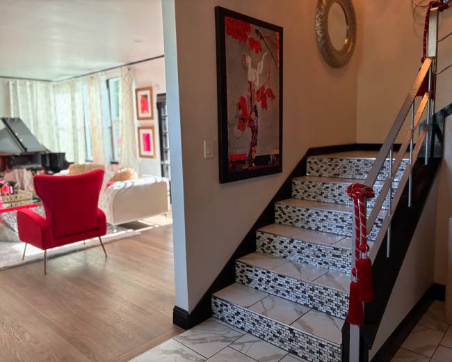 A staircase with decorative tiles leads up to a living area that features a grand piano and red accent furniture.