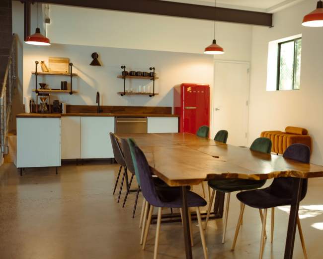 The image shows a modern kitchen and dining area featuring a wooden dining table, eight chairs, a red refrigerator, and minimalist decor.