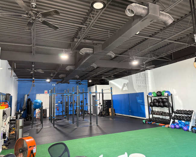 The image shows a well-equipped gym area featuring a blue and white color scheme, exercise equipment, and a section for strength training.