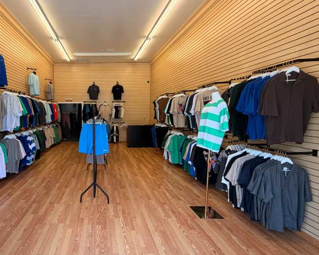 A clothing store displays a variety of shirts arranged neatly on racks along the walls and on a central stand.