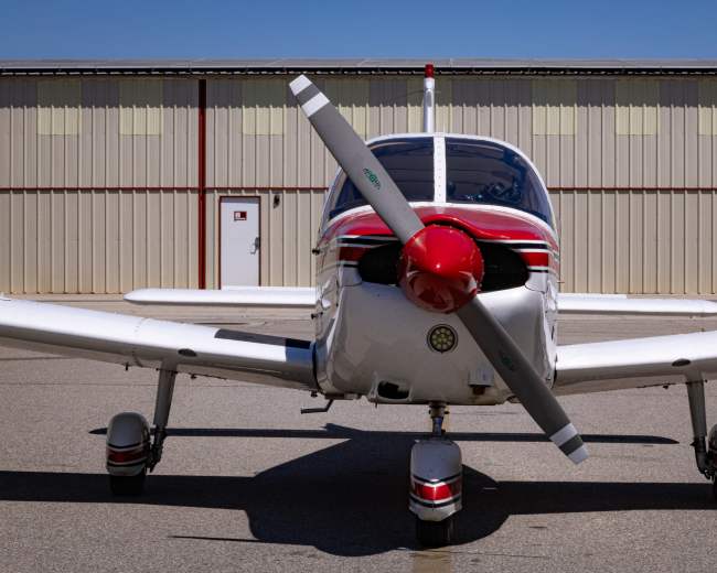 A small white and red aircraft with a propeller is parked in front of a hangar.