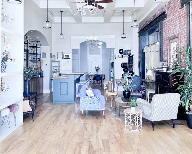 A spacious room with a high ceiling adorned with a chandelier and multiple light fixtures, featuring various seating arrangements and decorative plants.