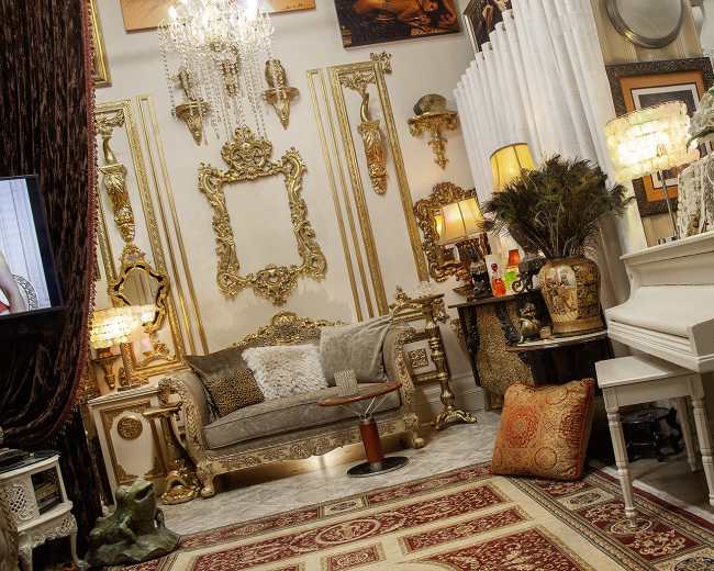 The image depicts a lavishly decorated room featuring ornate golden frames, a white piano, a plush sofa, and various decorative items arranged against a richly textured backdrop.