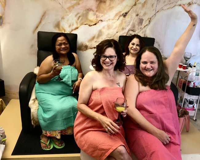 Four women in colorful spa robes pose together in a luxurious spa setting with "Spoiled Royal" decor in the background.