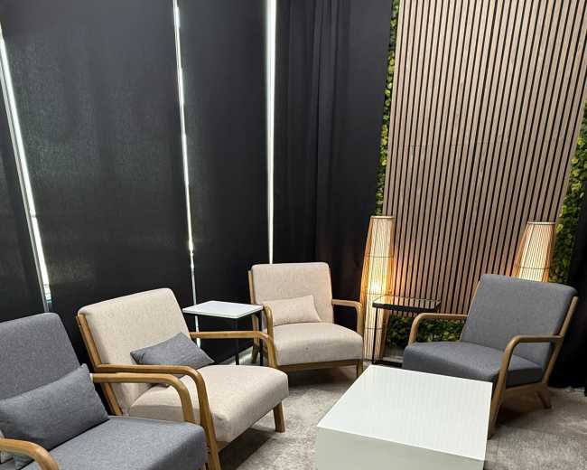 The image shows a seating area with four chairs and a coffee table, set against a backdrop of black curtains and a vertical wooden slat feature.