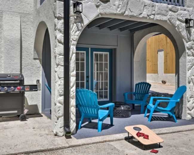 The image shows a patio area featuring a barbecue grill, blue outdoor chairs, and a bean bag toss game.