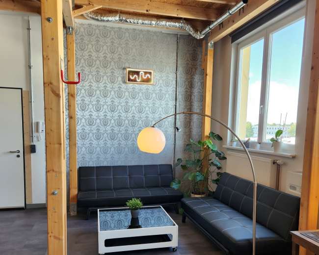 A modern lounge area with two black sofas, a round floor lamp, a coffee table, and greenery, set against a patterned wall and large windows.