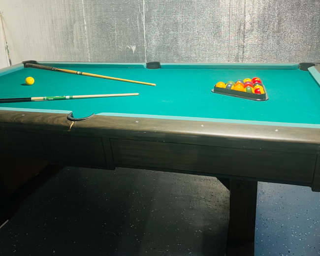 A pool table with a rack of colored balls sits in a dimly lit basement.