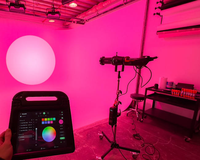 A pink-walled studio features a large illuminated circular light, with a control panel being held in front.
