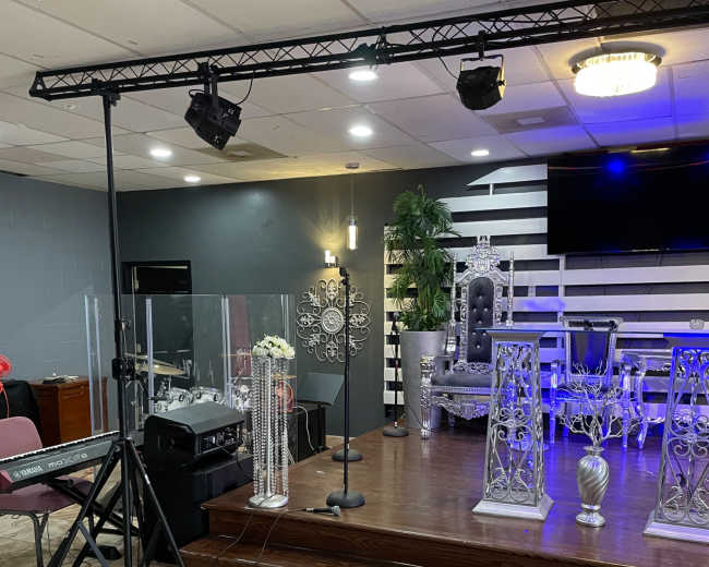 The image shows a stage setup with decorative chairs, a microphone stand, and a keyboard in a well-lit venue.