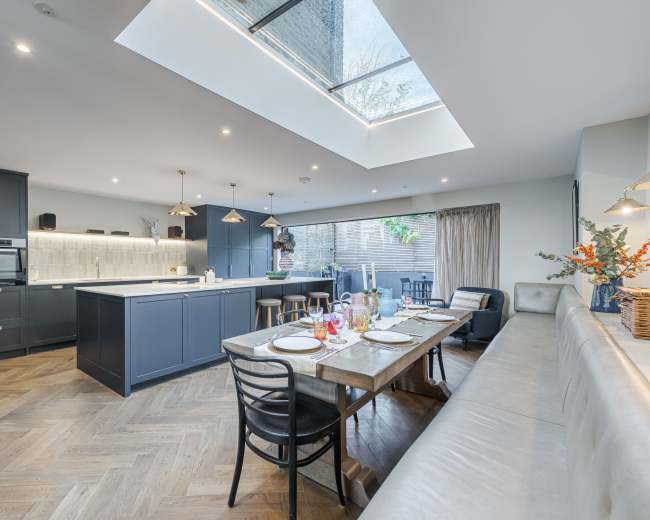 A modern kitchen features a large island with bar stools, a dining table set for a meal, and a skylight illuminating the space.