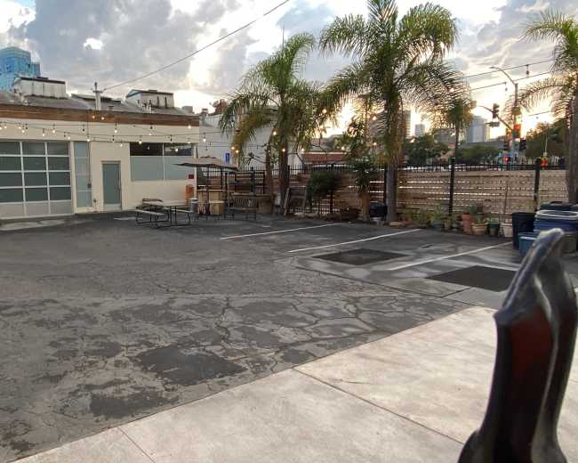 The image shows a sparse outdoor parking area with a concrete surface, string lights overhead, and a few palm trees in the background.