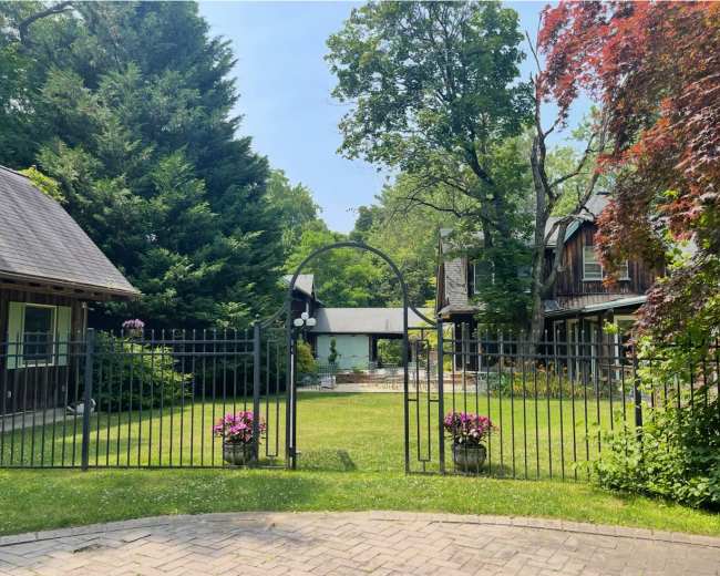 A wrought-iron gate opens to a landscaped courtyard surrounded by greenery and buildings.