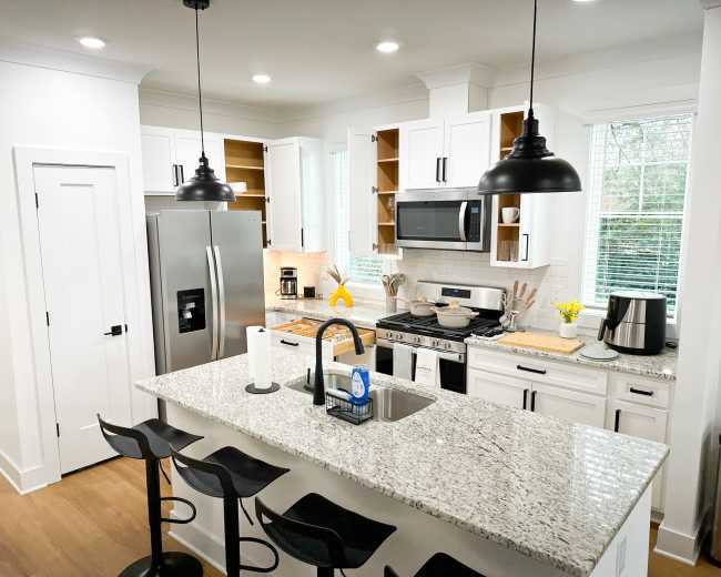 A modern kitchen features white cabinets, stainless steel appliances, and a large granite island with bar stools.