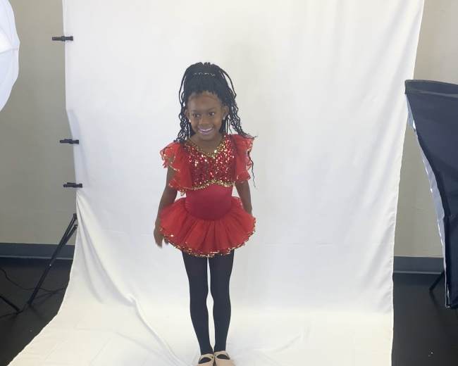 A young girl in a red sequined dance costume poses in front of a white backdrop.