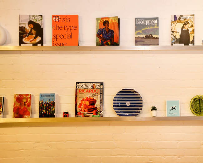 Shelves display a variety of books, magazines, and decorative items against a white brick wall.