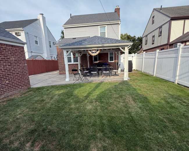 The image shows a backyard with a gazebo and a patio set, surrounded by a neatly trimmed lawn and residential homes.