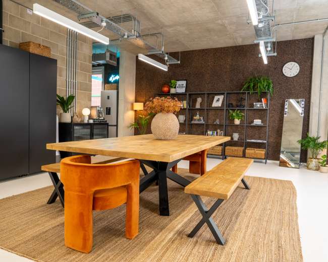 The image shows a modern dining area featuring a wooden table with benches, a round vase, and black storage cabinets against a textured wall.
