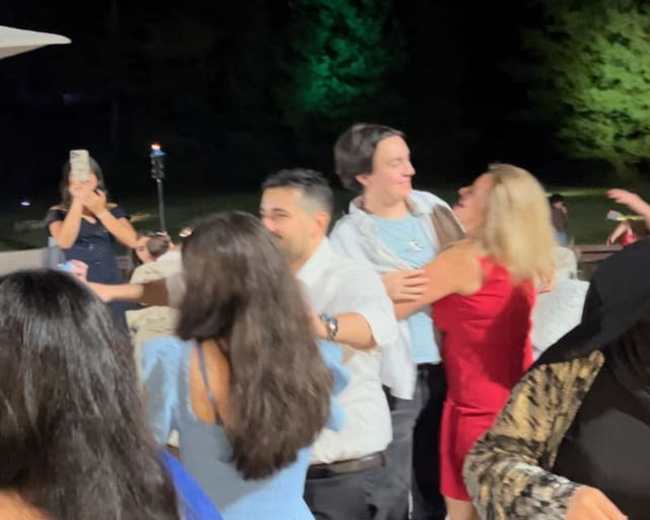 A group of people is dancing and socializing at an outdoor event in the evening.