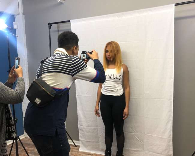 A photographer captures a model posing against a white backdrop in a studio.
