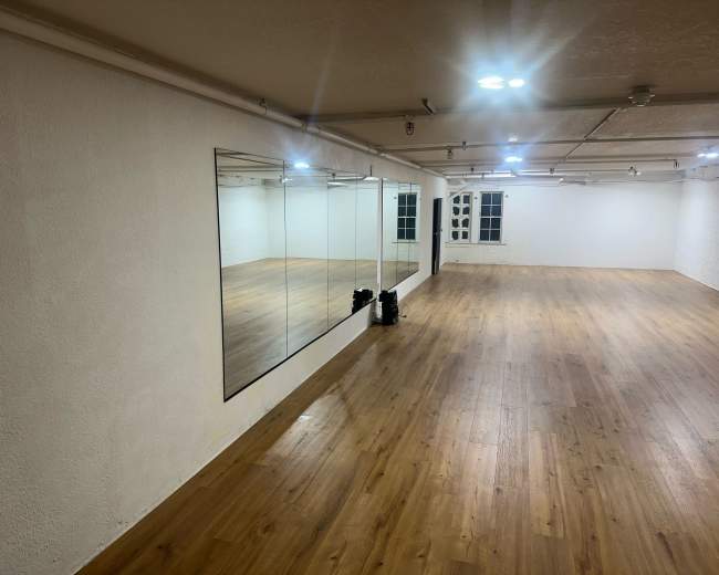 The image shows an empty dance studio with wooden flooring and mirrors along one wall.