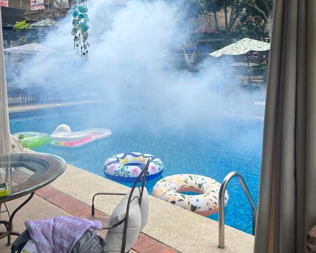 A pool area is visible, surrounded by colorful inflatable floats, with a blue mist hovering above the water.