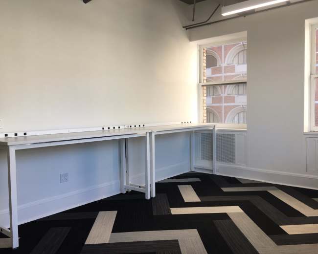 A bright, minimalist room with two white tables against a wall and a patterned black and gray carpet.