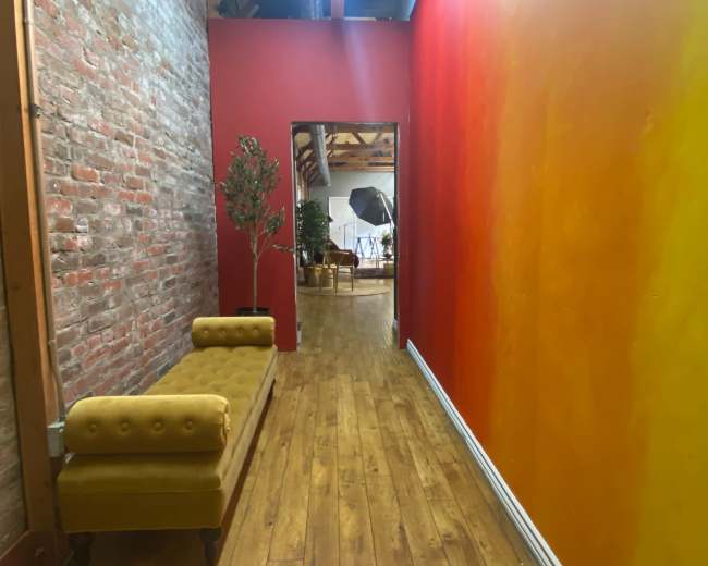 A narrow hallway features a brick wall on one side and a gradient orange wall on the other, with a yellow bench along the brick side.
