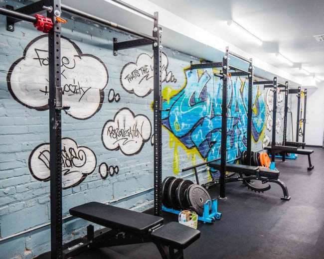 A gym interior with weightlifting equipment and colorful graffiti on the walls.